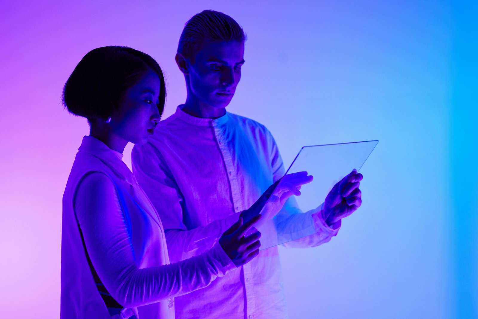 Two adults engaging with transparent screen, illuminated by vibrant purple and blue lights.